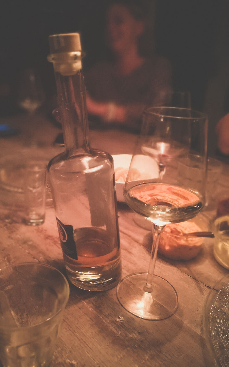 Heel veel lege glazen op een houten tafel en ene fles drunken mel die bijna leeg is.